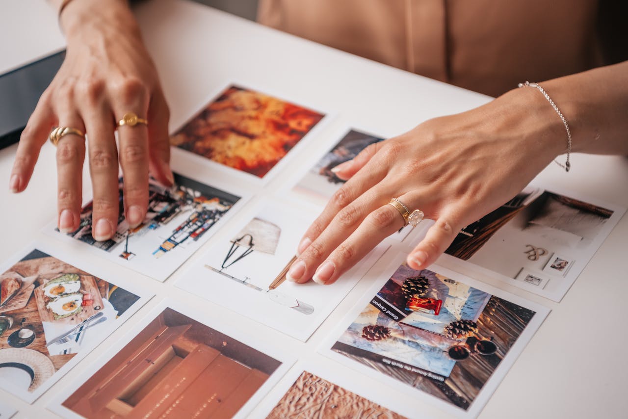 Hands arranging photo prints on a table, showcasing creativity and organization in content creation.